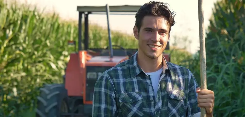 Jeune homme devant un tracteur dans un champ